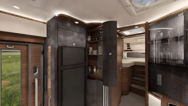 Luxuriöse Innenausstattung des Carthago Chic E-Line-Wohnmobils mit dunklen Holzschränken, Einbaugeräten, offenen Regalen mit Glaswaren und Getränken sowie einem gemütlichen Schlafbereich im hinteren Teil. Durch die Fenster und das Oberlicht fällt natürliches Licht herein.
