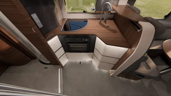 Moderne Wohnmobilküche im Carthago Chic E Line mit Arbeitsplatten aus Holz, Einbaukocher und -backofen, Spüle, weißen Schränken und grauem Bodenbelag. Ein Fenster über der Spüle lässt Tageslicht herein. Abgerundete Kanten und gemütliche Designelemente sind zu erkennen.