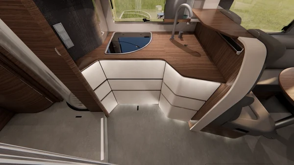 Eine moderne Wohnmobilküche mit Arbeitsplatten aus Holz, eingebauter Spüle, Schränken, Unterbauleuchten und einem geschwungenen Design – ein Paradebeispiel für den raffinierten Stil der Carthago Chic E-Linie. Über der Spüle befinden sich eine Armatur und ein Fenster, und auf der rechten Seite sind ein Teil des Tisches und eine Sitzgelegenheit zu sehen.
