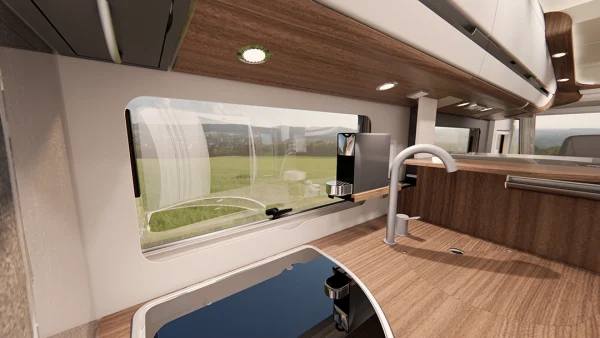 Moderne Wohnmobilküche mit Holzoptik, Arbeitsplatte, Spüle, Kochfeld und Kaffeemaschine. Durch das große Fenster blickt man auf eine grüne Wiese und Hügel, die den Raum mit Tageslicht durchfluten – eine einladende Atmosphäre, die den Luxus der Carthago Chic e-line perfekt zur Geltung bringt.
