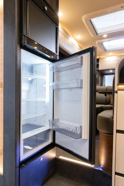 Ein leerer, offener Kühlschrank mit durchsichtigen Einlegeböden und Türfächern im Innenraum eines modernen, gut beleuchteten Carthago Liner-for-Two-Wohnmobils oder -Wohnwagens.