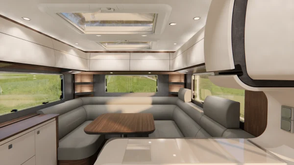 Moderne Wohnmobil-Innenausstattung mit hellen Sitzgelegenheiten rund um einen Holztisch, großen Fenstern mit Blick ins Grüne, Hängeschränken und Oberlichtern, die Tageslicht hereinlassen. Das Design dieses Carthago Liner for Two ist elegant und geräumig.