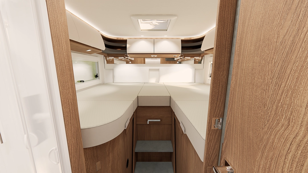 Innenansicht eines modernen Schlafzimmers im Carthago C2-Tourer-Wohnmobil mit zwei Einzelbetten, Holzschränken, Stauraum an der Decke, Regalen und einem Dachfenster. Neutrale Farbtöne und ein klares Design sorgen für ein geräumiges Ambiente. Die Aufnahme wurde von der Tür aus in Richtung der Betten aufgenommen.