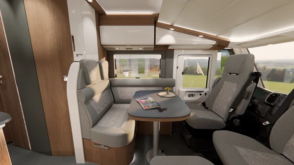 Moderner Wohnmobil-Innenraum mit grauen Sitzen, einem Esstisch mit Zeitschriften und einer Blume, großen Fenstern und hellen Holzschränken. Durch die Fenster ist draußen eine Wiese zu sehen – ein Beispiel für den Komfort und das elegante Design, das für den Carthago C2-Tourer typisch ist.