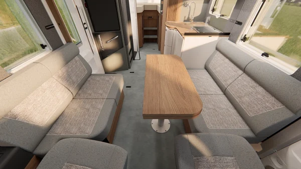 Innenraum eines Carthago C2-Tourer-Wohnmobils mit zwei langen gepolsterten Sitzbänken, einem Holztisch in der Mitte, einer kleinen Küchenzeile mit Spüle und einem Kühlschrank, alles in neutralen Farben gehalten.