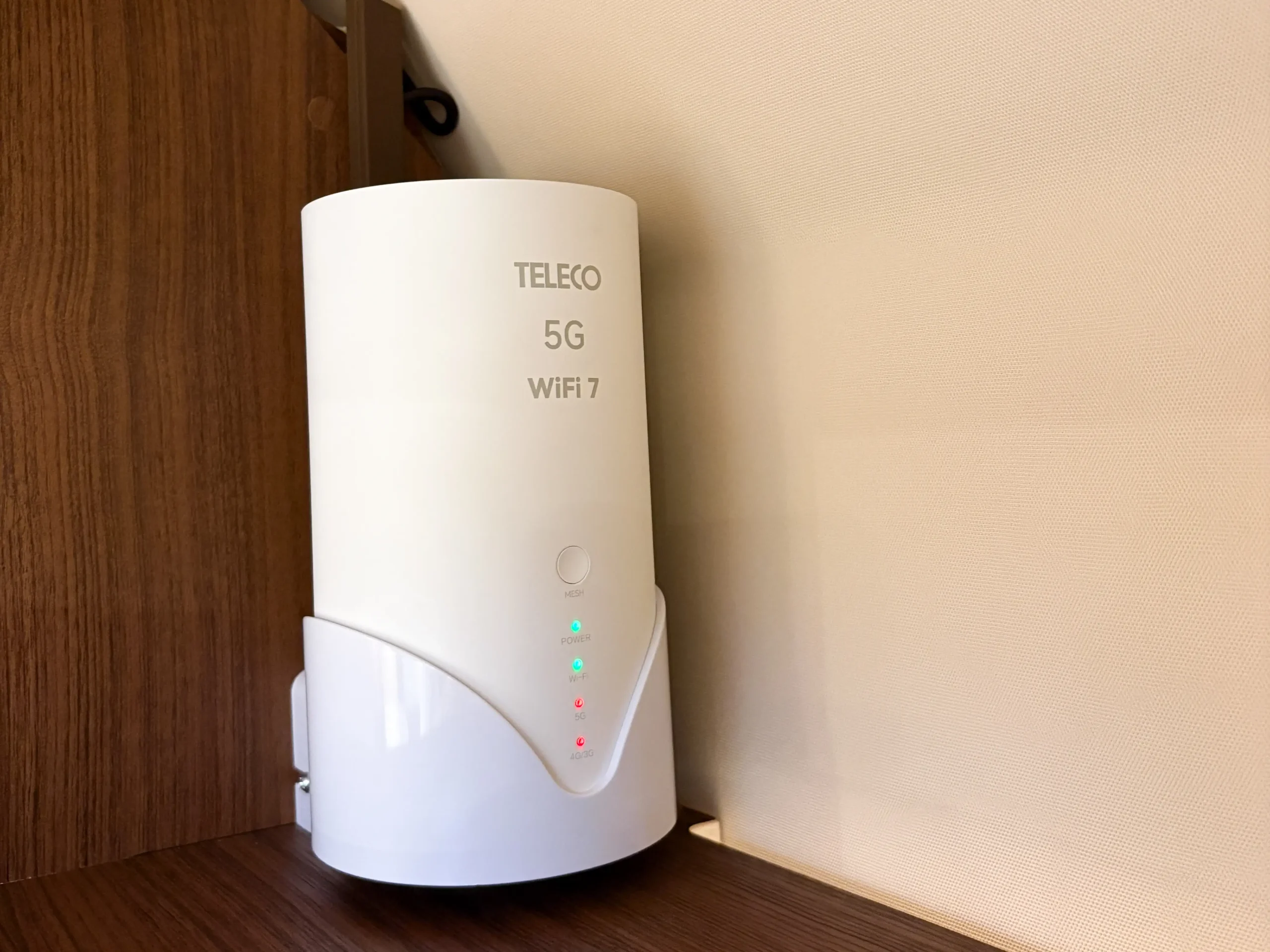 Ein weißer TELECO 5G WiFi 7-Router mit Kontrollleuchten steht auf einem Holzregal vor einer beigen Wand und fügt sich perfekt in die moderne Innenausstattung eines Carthago Liner for Two ein.