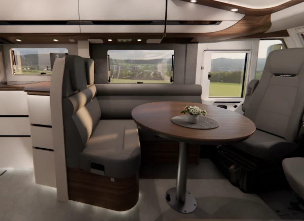 Moderne Wohnmobil-Innenausstattung mit rundem Tisch, gepolsterter Sitzbank, drehbarem Kapitänsstuhl, Dekor in Weiß und Holz, Arbeitsplatte sowie Blick aus dem Fenster auf grüne Felder und Berge. Ein kleines Tischdekor ziert den Tisch in dieser luxuriösen Carthago Chic E-Line-Umgebung.