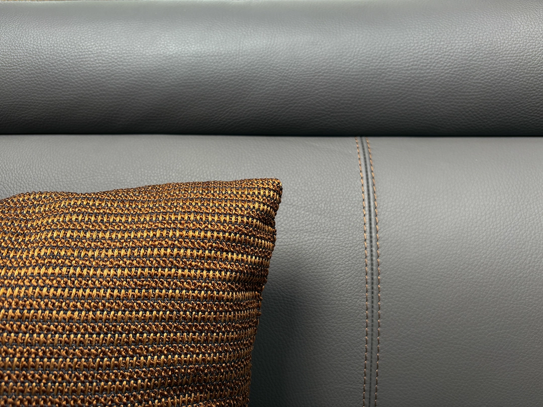 Eine Nahaufnahme eines braunen, strukturierten Kissens auf einem grauen Ledersofa mit sichtbaren Nähten, die das raffinierte Innendesign einfängt, das an die luxuriösen Wohnmobile der Carthago Chic e Line erinnert.