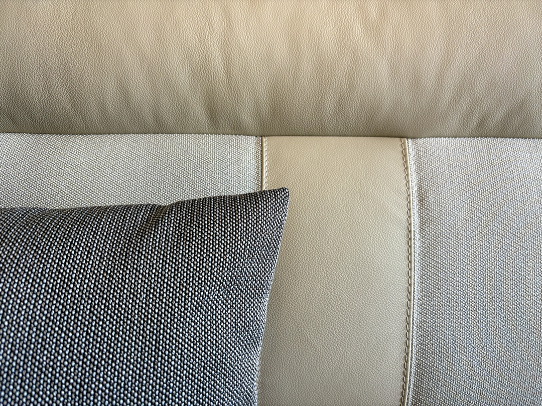 Nahaufnahme eines hellbeigen Ledersofas mit sichtbaren Nähten, auf dessen linker Seite ein dunkelgraues, strukturiertes Kissen platziert ist – ein eleganter Akzent, der an die raffinierte Innenausstattung eines Carthago Chic E Line erinnert.