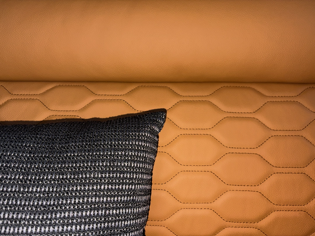Nahaufnahme eines strukturierten schwarz-weißen Kissens auf einem braunen Ledersofa mit gesteppten, geometrischen Mustern, die das elegante Ambiente des Interieurs einfangen, das an eine Carthago Chic E-Line erinnert.