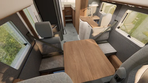 Innenraum eines modernen Carthago C2-Tourer-Wohnmobils mit einem Esstisch aus Holz, gepolsterten Sitzen mit Sicherheitsgurten, großen Fenstern und einem kompakten Küchenbereich mit Spüle, Schränken und viel Tageslicht.