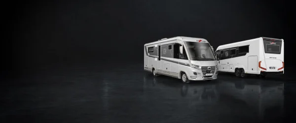 Zwei weiße Wohnmobile, darunter ein Carthago Liner for Two, stehen auf einer dunklen, glänzenden Fläche vor einem schwarzen Hintergrund. Ein Wohnmobil ist nach vorne ausgerichtet, während das andere sein Heck zeigt.