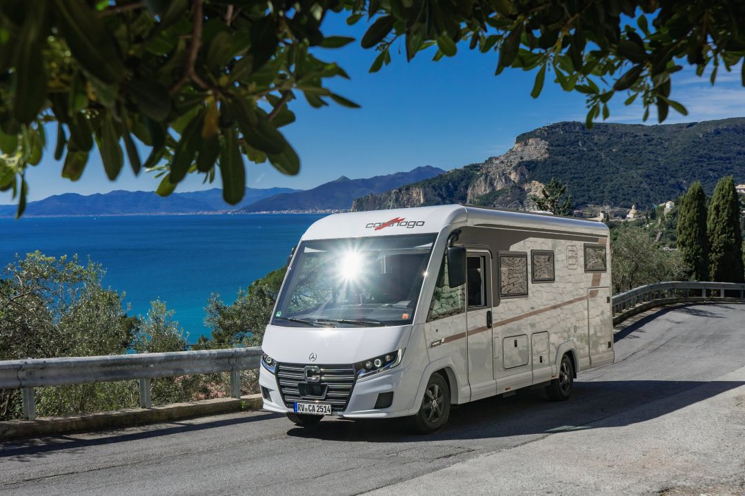 Ein weißes Carthago-Wohnmobil fährt auf einer Küstenstraße mit Blick auf das Meer in der Nähe eines Wohnmobilstellplatzes.
