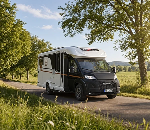 Ein schwarz-weißes, teilintegriertes Carthago C-Tourer-Wohnmobil fährt auf einer von Bäumen gesäumten Landstraße.