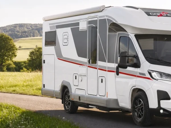 Ein weißes Wohnmobil vom Typ Carthago Chic C-Line T, das auf einer asphaltierten Straße neben einer Wiese geparkt ist.