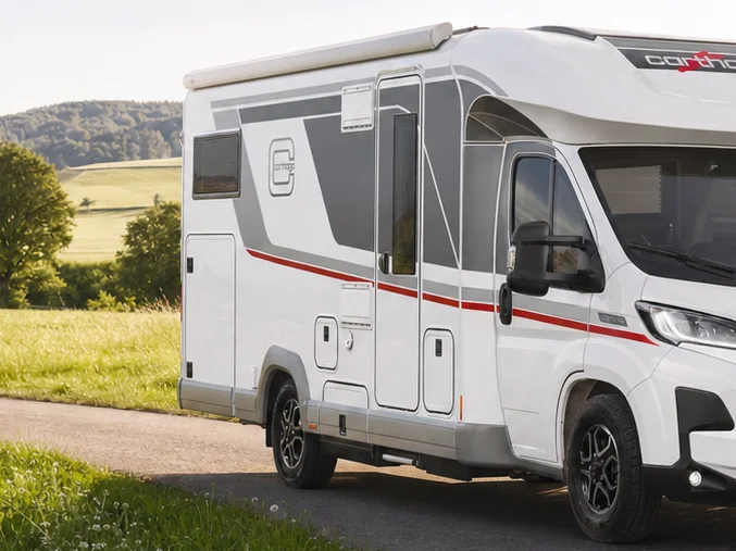 A white Carthago chic c-line T motorhome parked on a tarmac road next to a meadow.