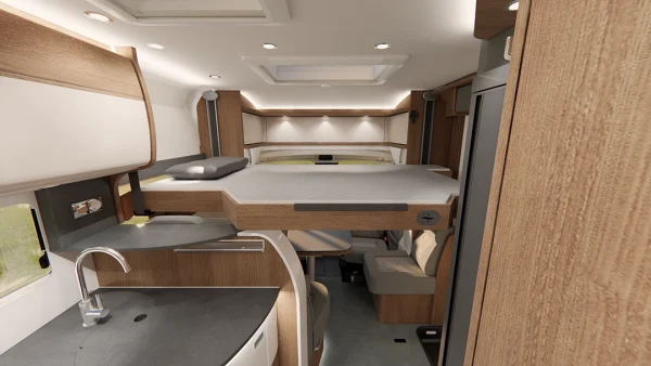 Innenraum eines halbintegrierten Wohnmobils vom Typ Carthago c-tourer, im Vordergrund eine Küchenzeile mit Spüle und darüber ein Klappbett über einem kleinen Essbereich.