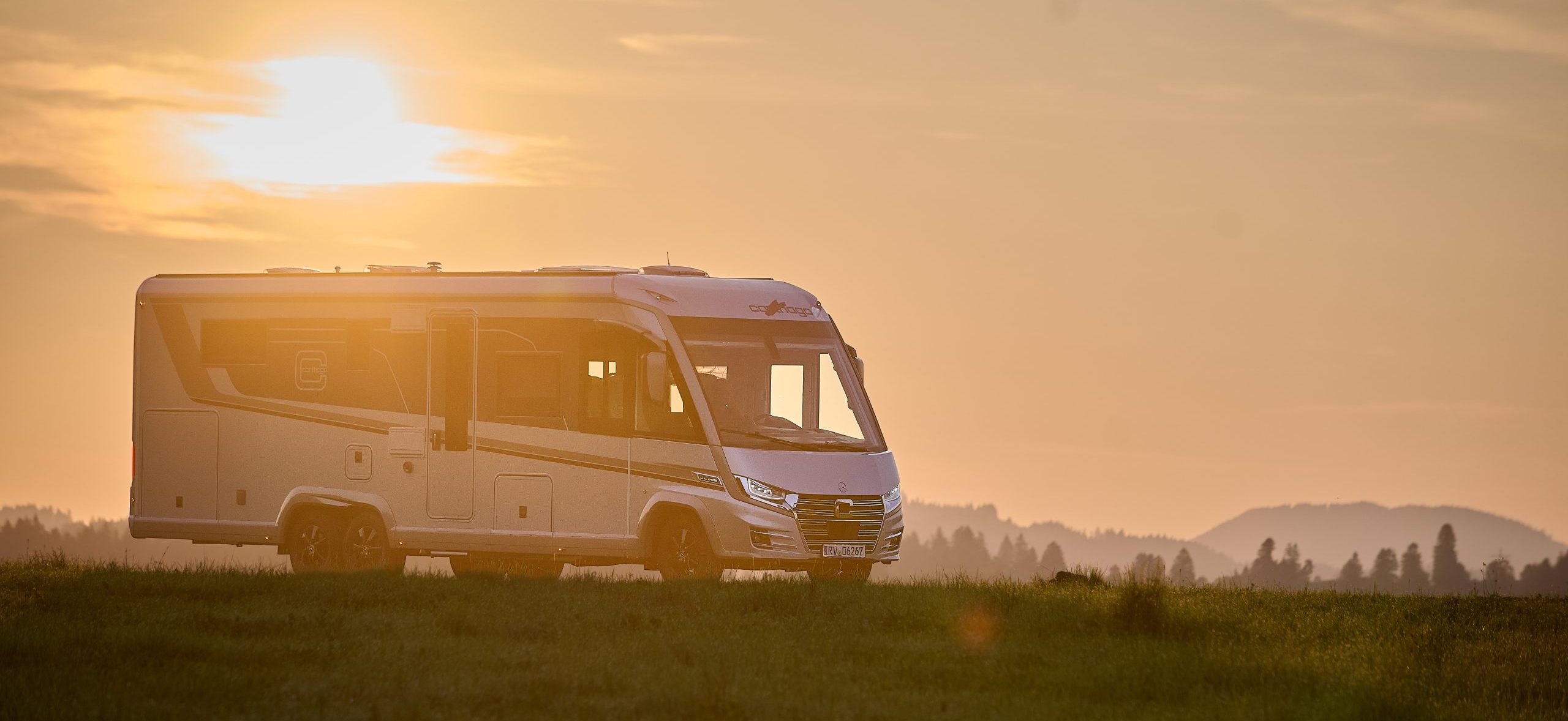 Un camper Carthago parcheggiato al tramonto in un’area di sosta per camper situata in un prato.