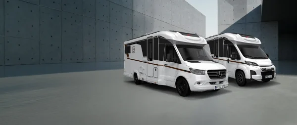Vor einer grauen Betonmauer standen zwei weiße Wohnmobile.