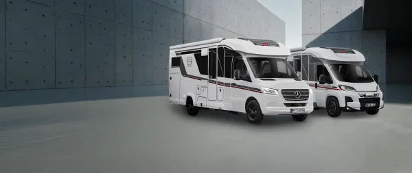 Zwei weiße Carthago-Wohnmobile standen vor einer grauen Betonmauer.