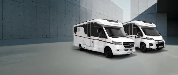 Zwei weiße Wohnmobile, die nebeneinander vor einer grauen Betonmauer geparkt sind.