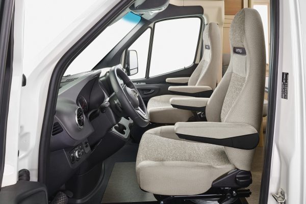 Innenraum eines teilintegrierten Carthago c-tourer-Wohnmobils mit zwei hellen Kapitänsstühlen und dem Armaturenbrett mit Lenkrad.