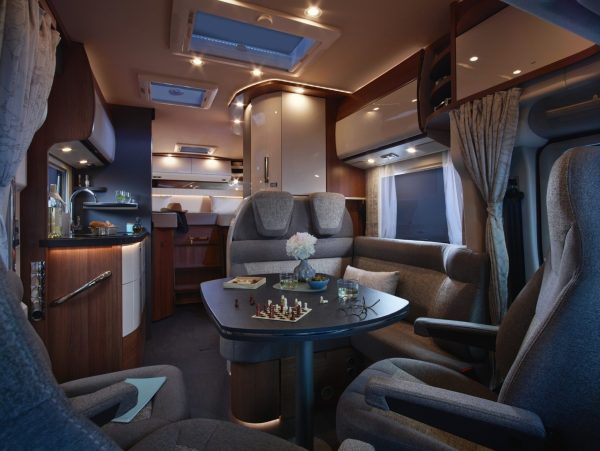 Innenraum eines teilintegrierten Carthago c-tourer-Wohnmobils mit einer Essecke, in der ein Tisch für eine Schachpartie gedeckt ist, angrenzend an eine kleine Küchenzeile.